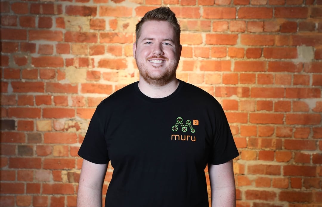 Josh smiling standing in front of a brick wall.