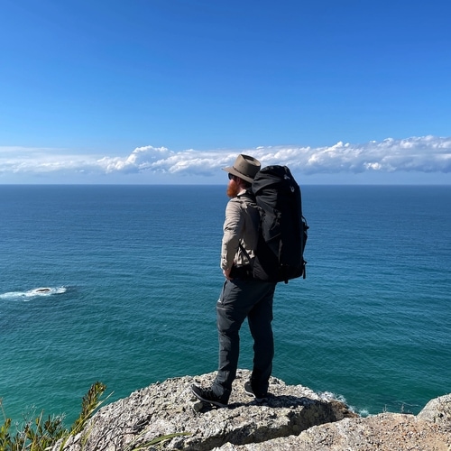 Josh in a hiking outfit standing on a cliff edge overlooking the ocean.