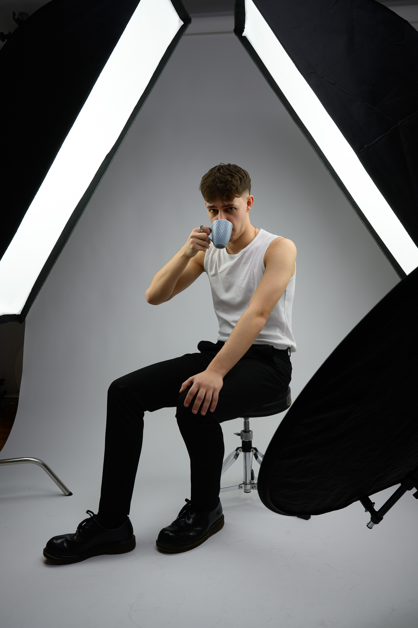 Mężczyzna siedzi w studiu fotograficznym i pije kawę. Dookoła widać rozstawione oświetlenie studyjne