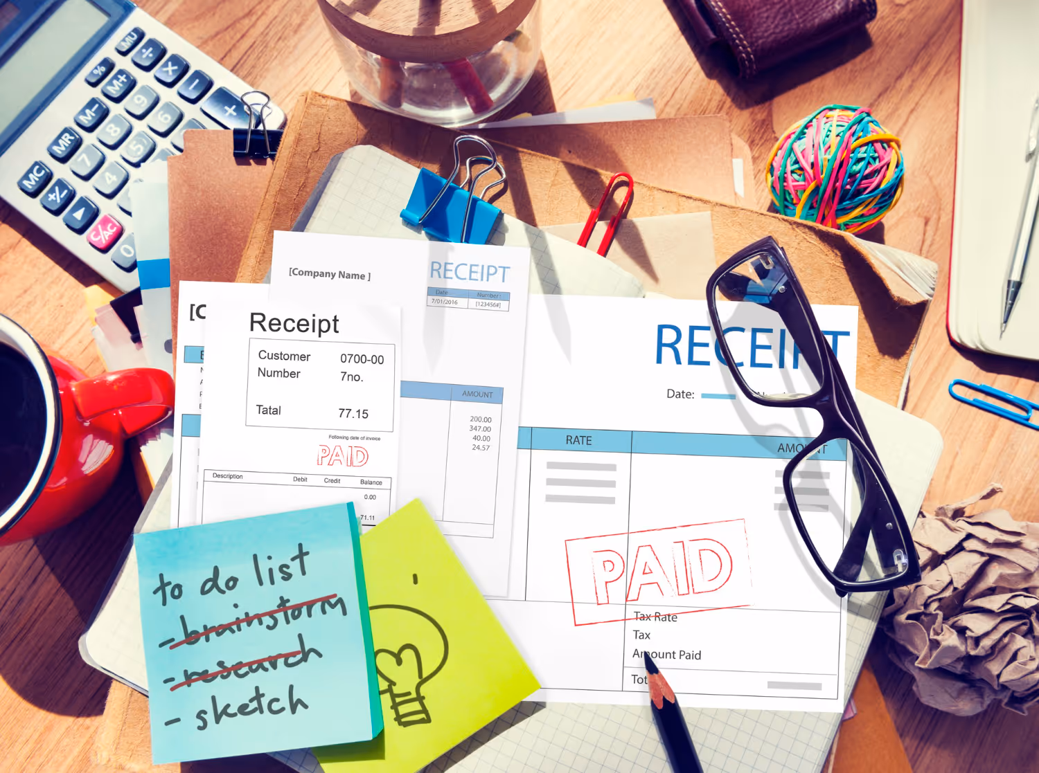 Sticky note of to do list, with receipts and calculators on the table