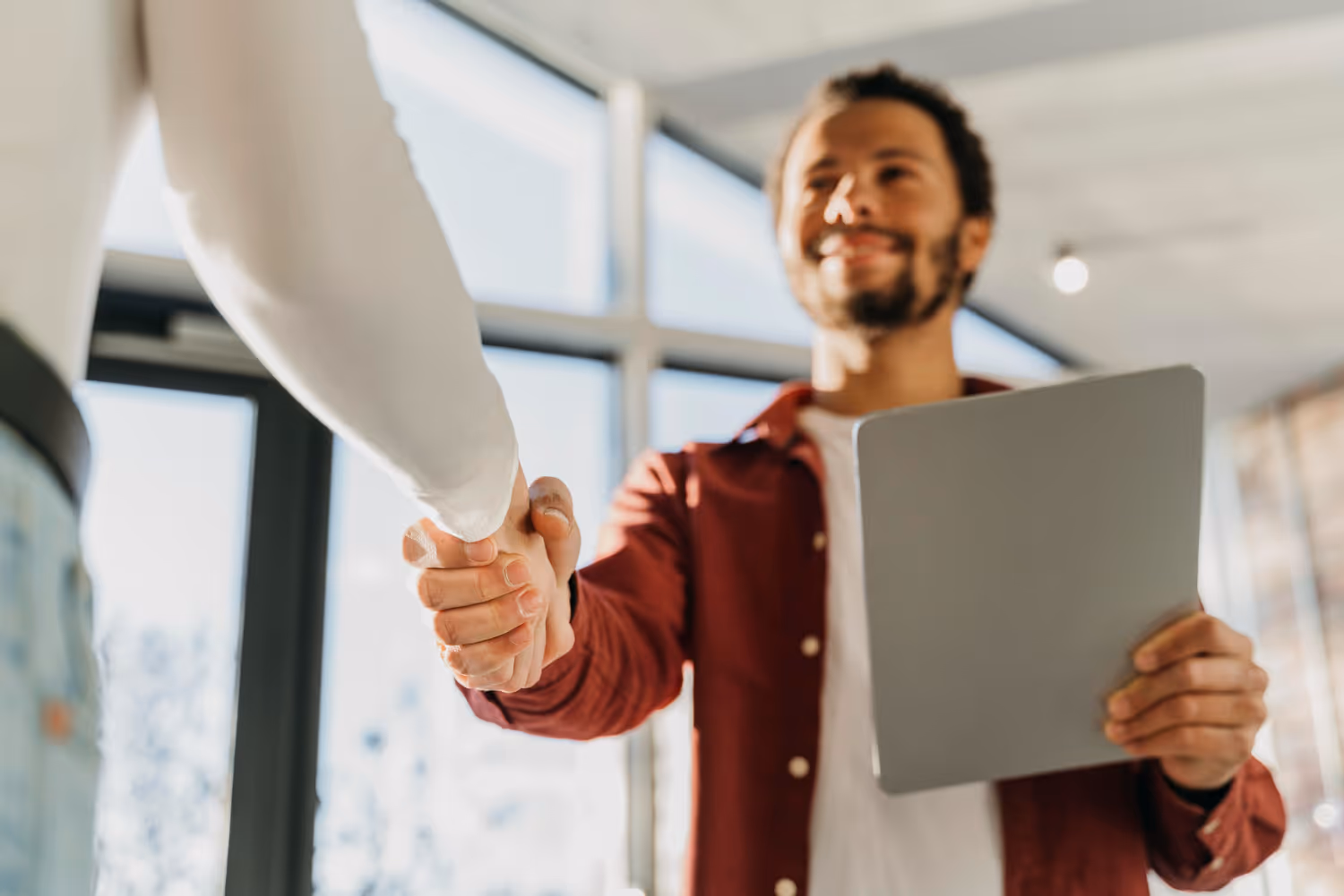 Employer holding a tablet, shaking hands with his remote employee