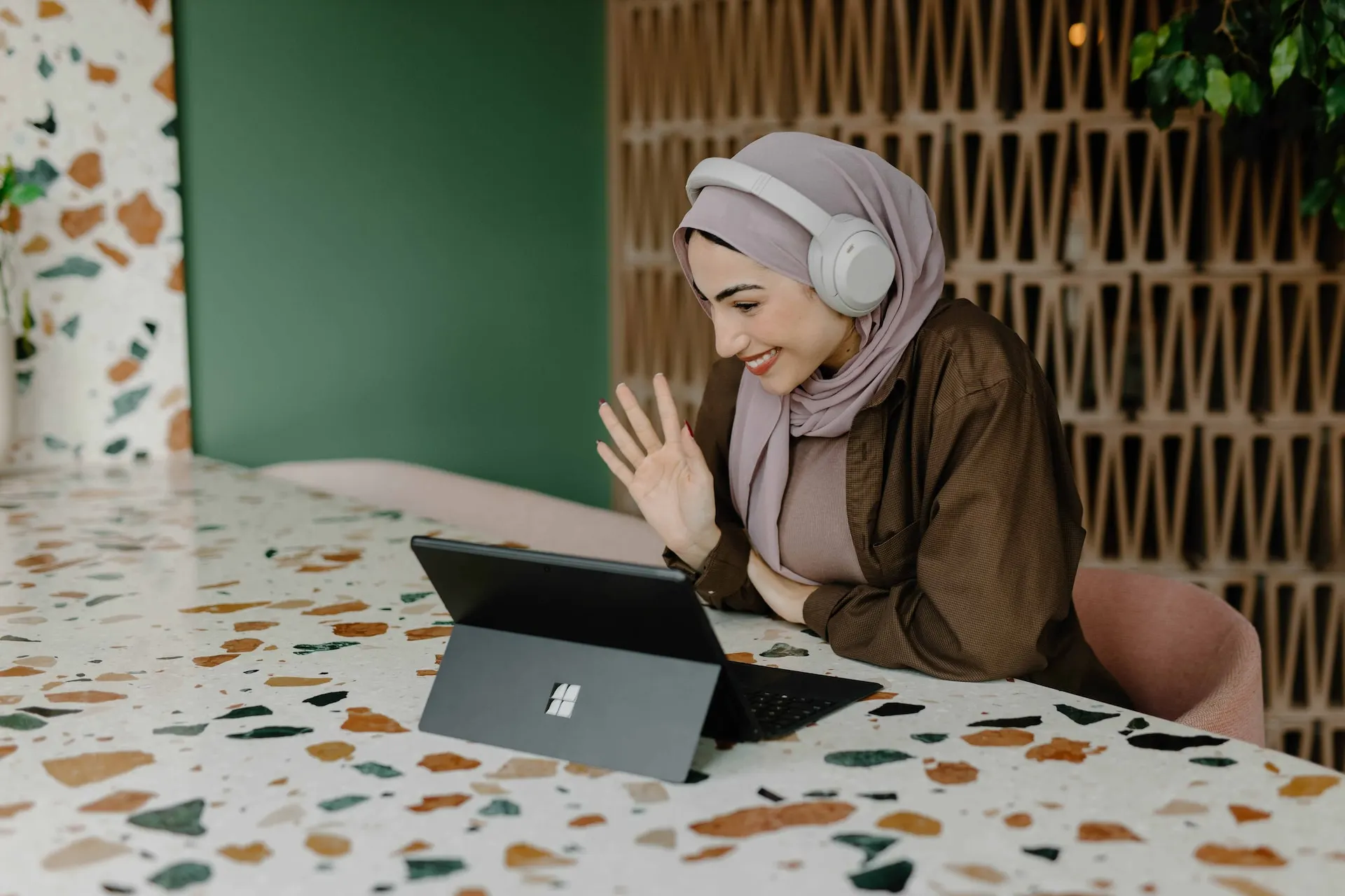 Asynchronous employee working at home, wearing headphones, waving and smiling at laptop