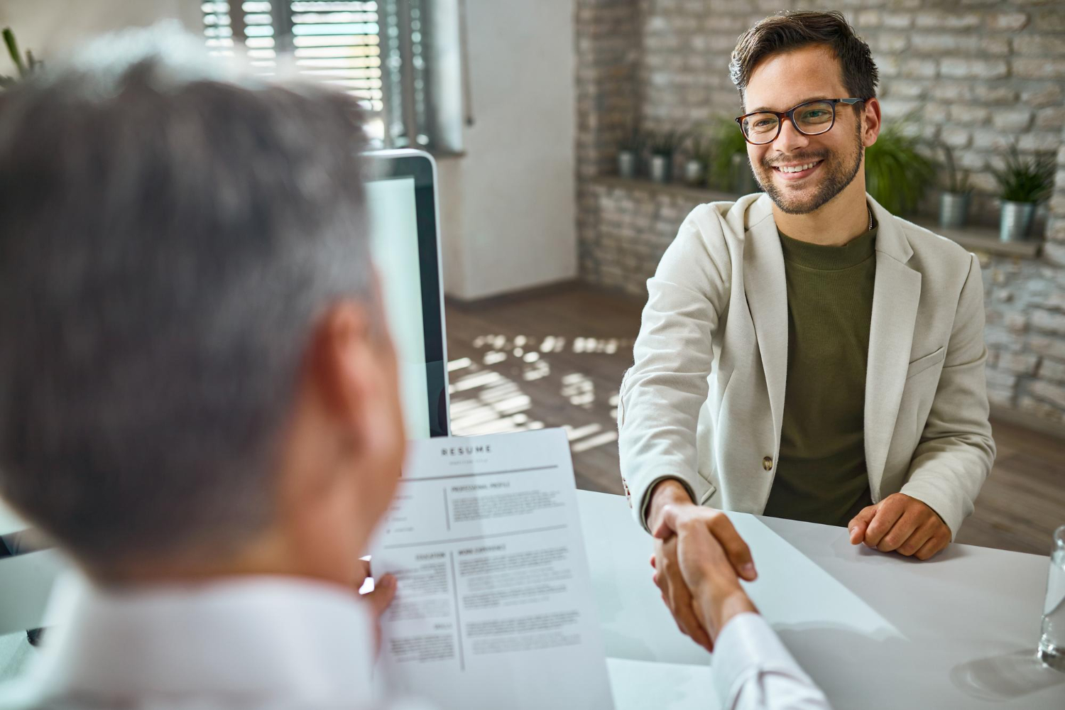 Candidate applying to a job is smiling at the employer who is holding his resume