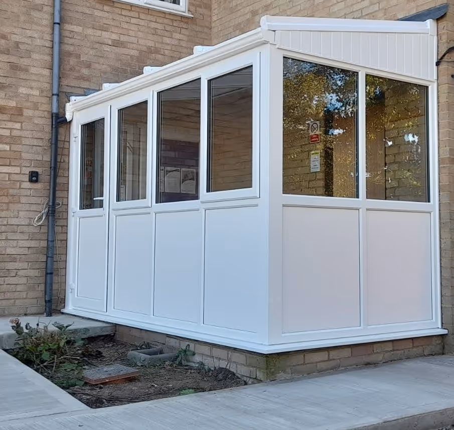 A white, rectangular conservatory is attached to a brick house, featuring large windows and a glass roof.