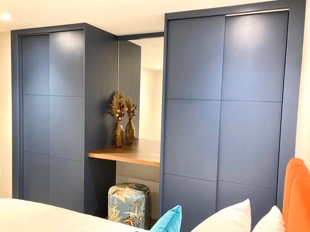 Closed blue sliding closet doors with a wooden table inside. Dried plants in a vase on the table.