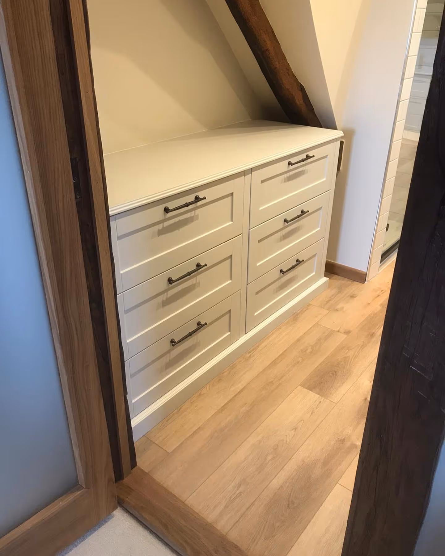 Built-in white dresser with eight drawers, situated in a room with wooden floors and beams.