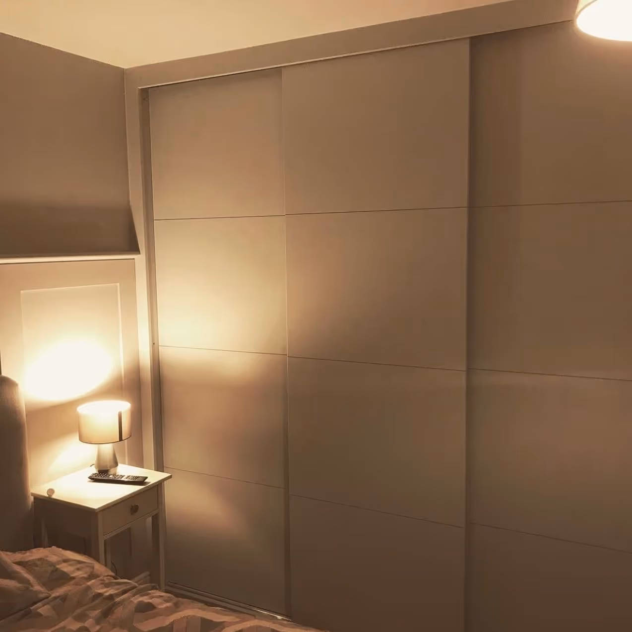A bedroom with a lamp on a nightstand, softly lighting up the room.