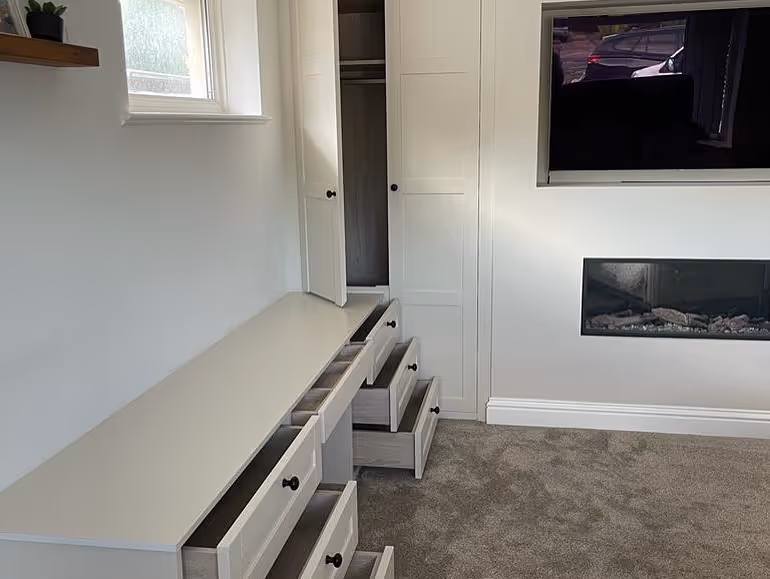Open drawers and a partially open wardrobe in a white, modern bedroom setup.