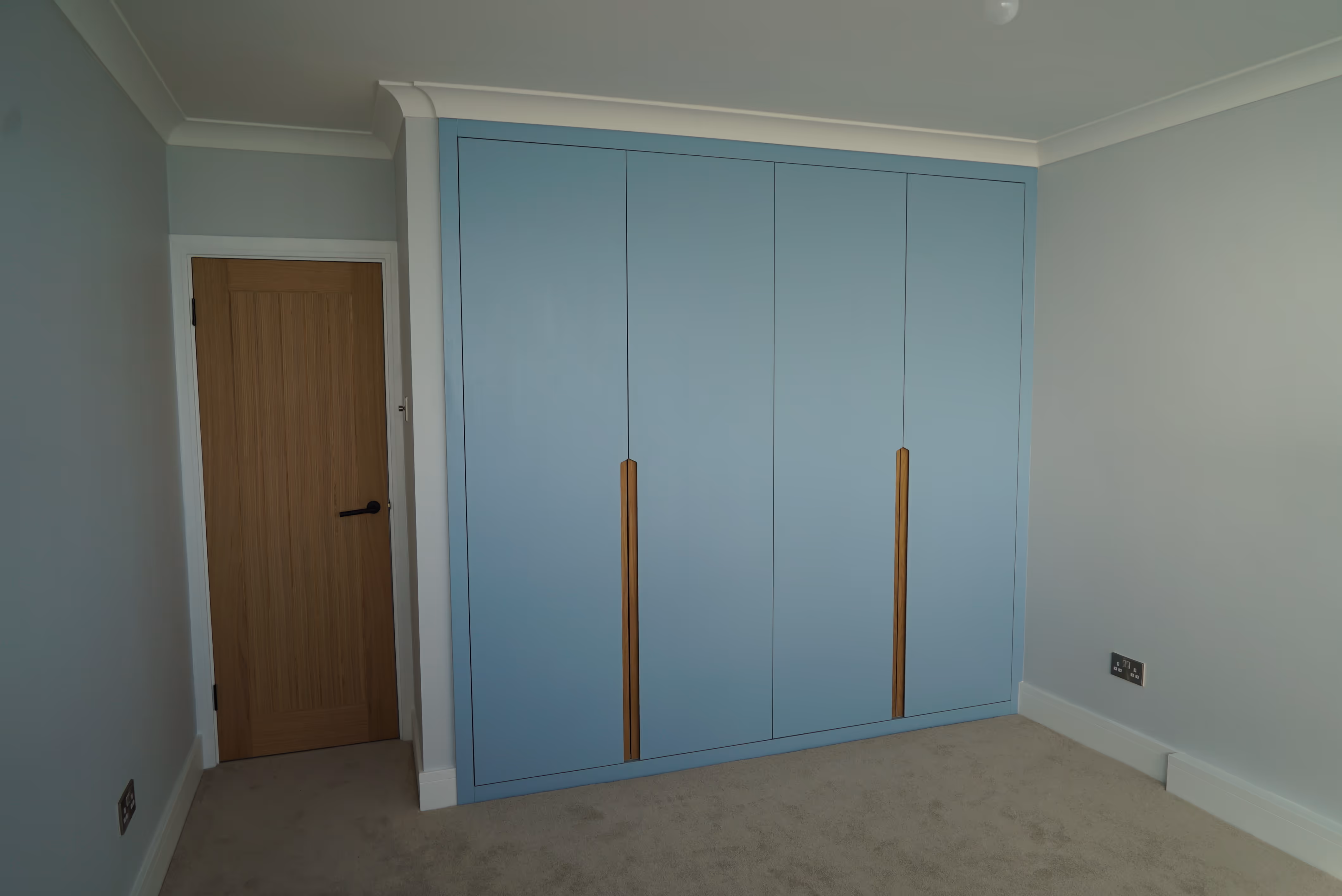 Light blue wardrobe with wooden handles next to a closed wooden door in a carpeted room.