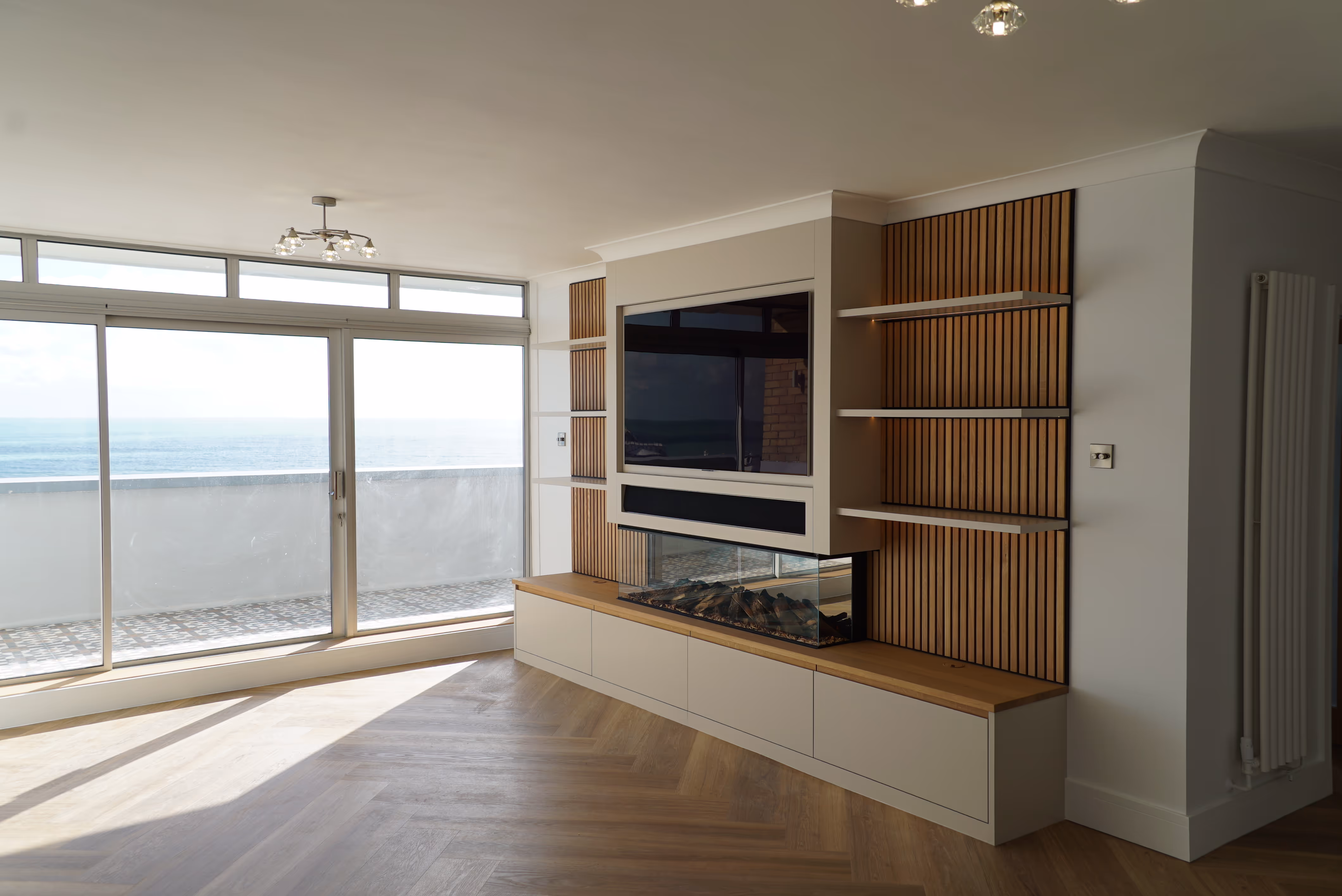 A modern living room with a large window and built-in shelves, overlooking the ocean.