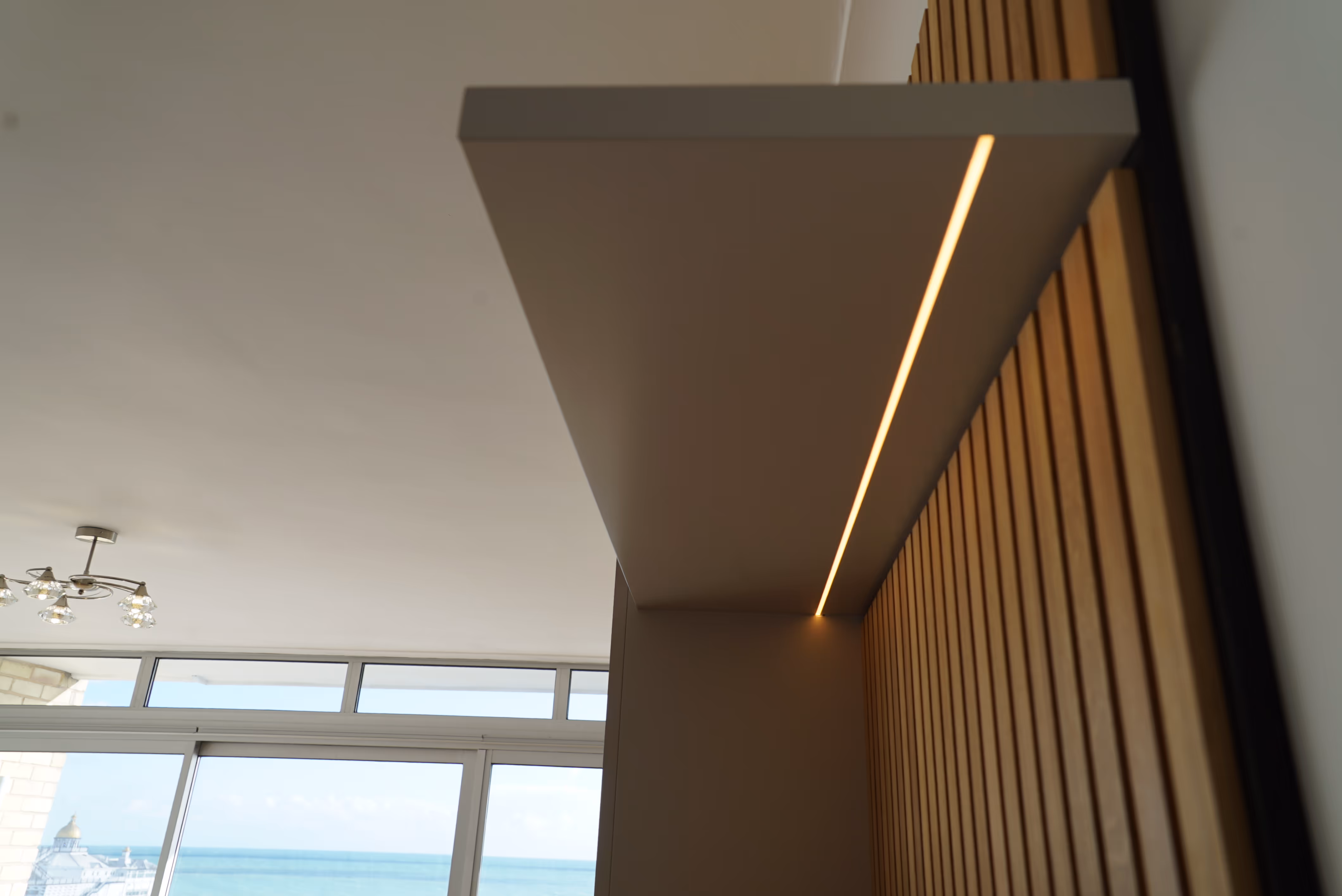 A modern ceiling light fixture is illuminated in a room with large windows overlooking the sea.