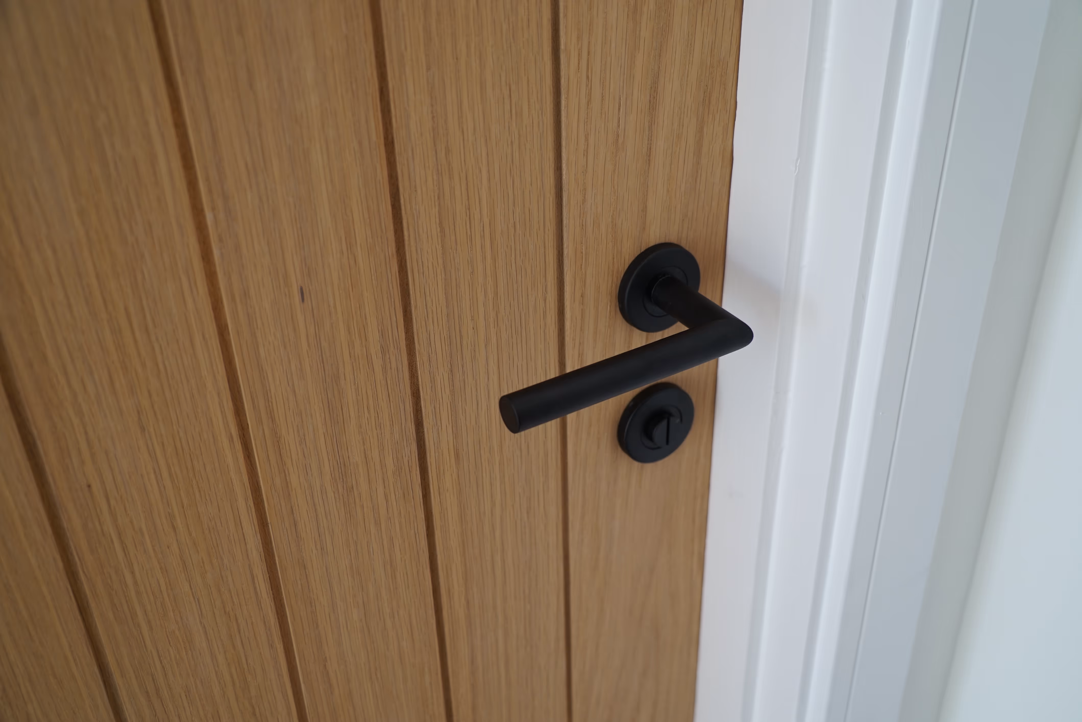 Wooden door with a black handle and lock, shown close-up from the side.