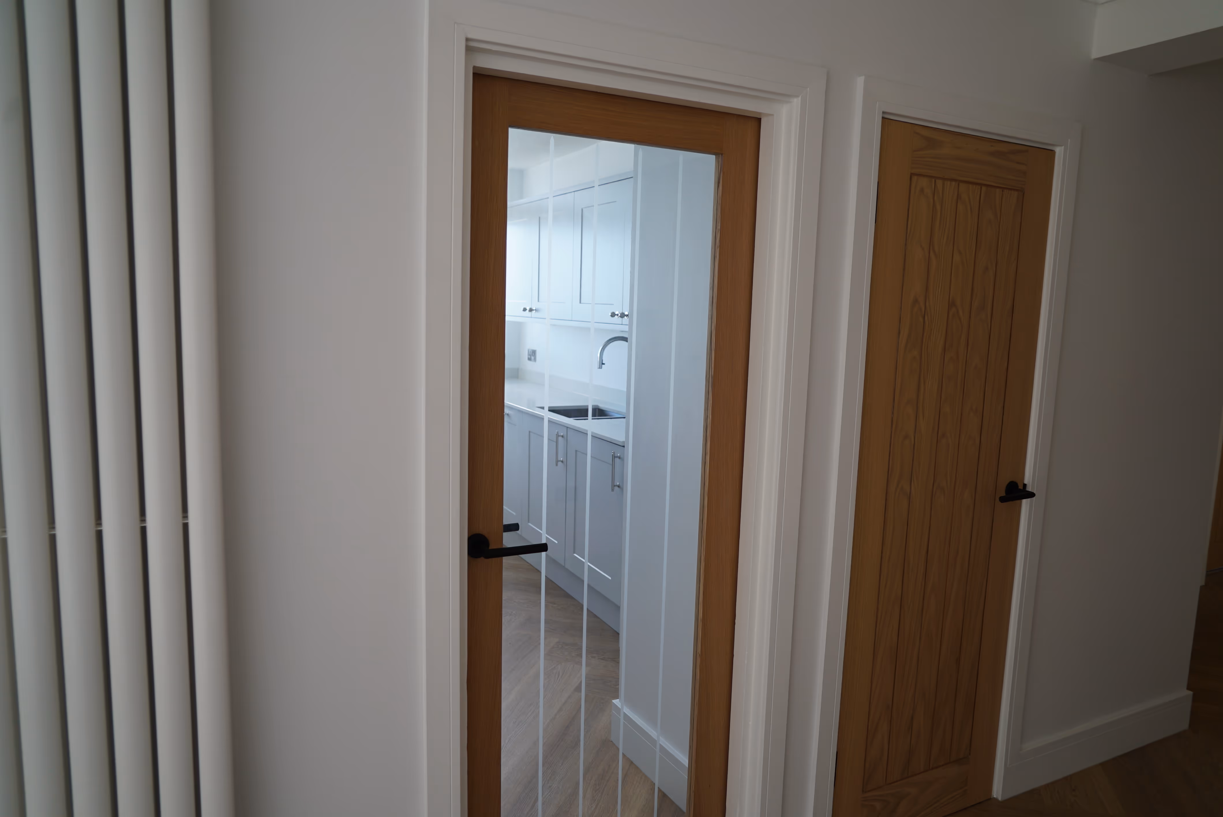 Glass door opens to a bright, modern kitchen with white cabinets and wooden flooring.
