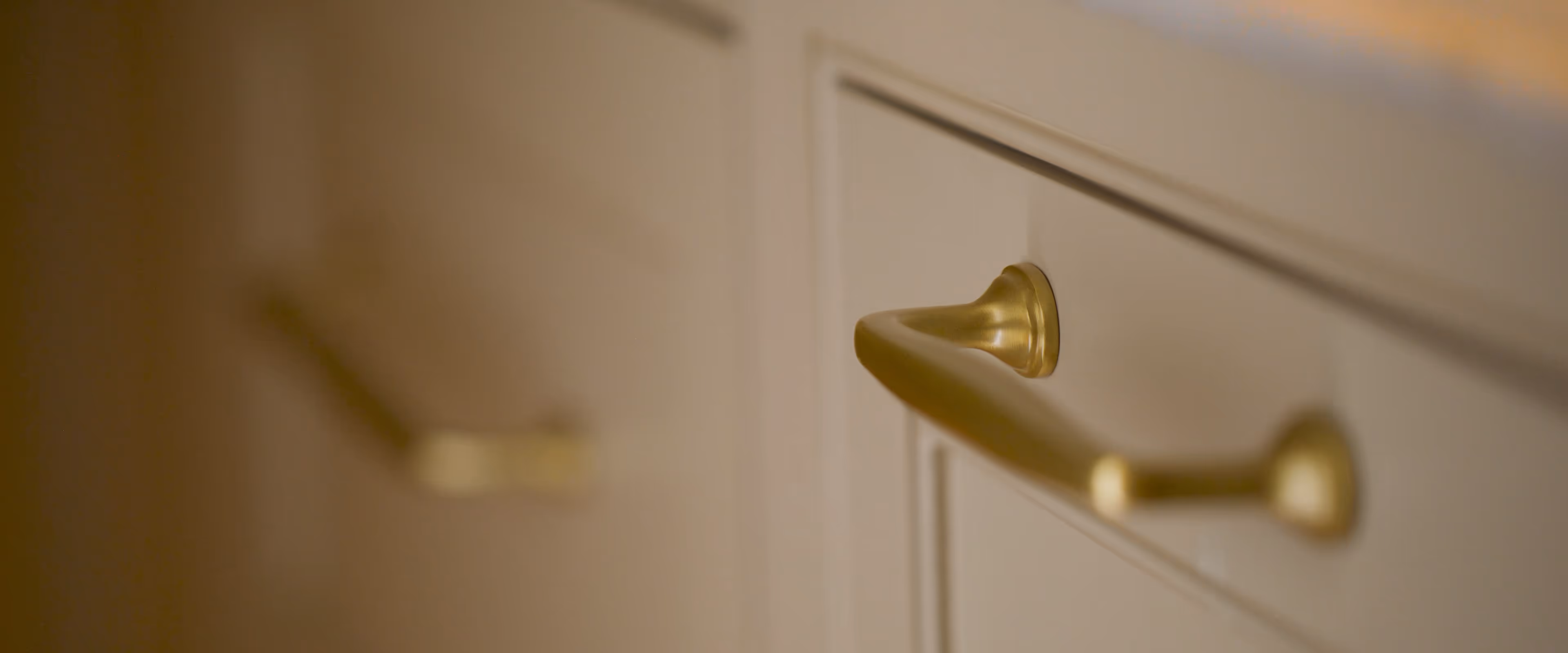Close-up of a golden handle on a cream-colored cabinet drawer.