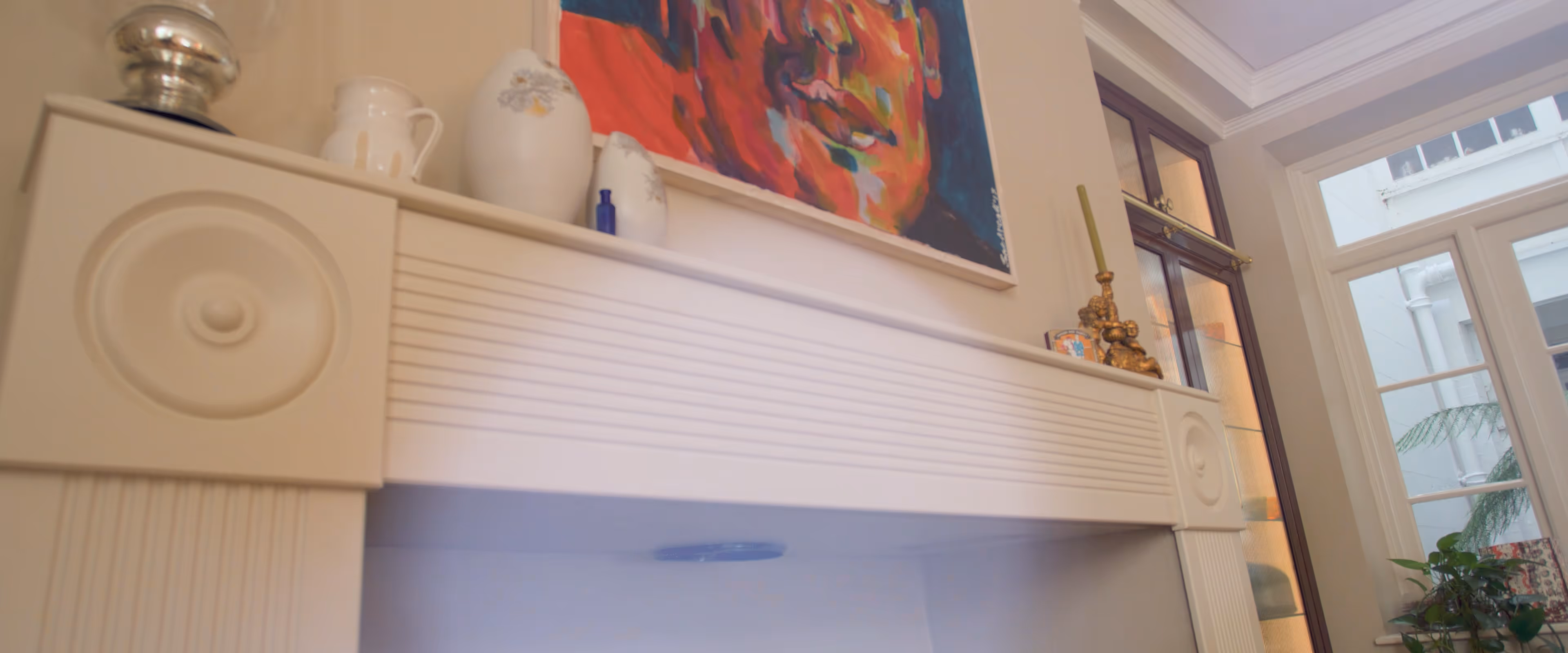 A mantle with a colorful face painting above and decorative items, including a vase and candleholder.