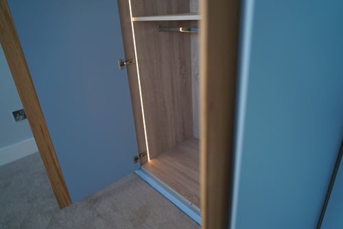 An open blue wardrobe shows empty wooden shelves and a hanging rod inside.