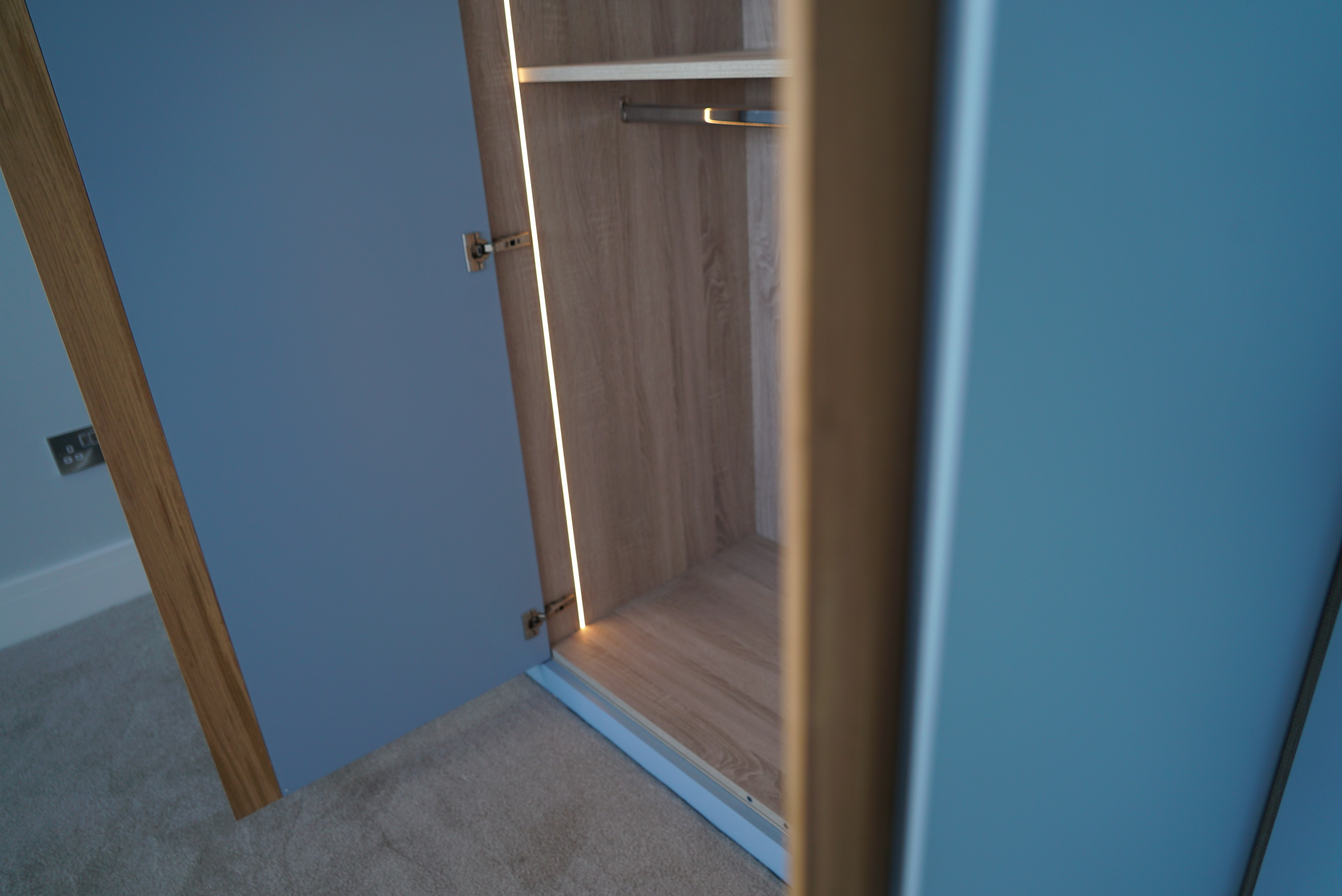 An open blue wardrobe shows empty wooden shelves and a hanging rod inside.