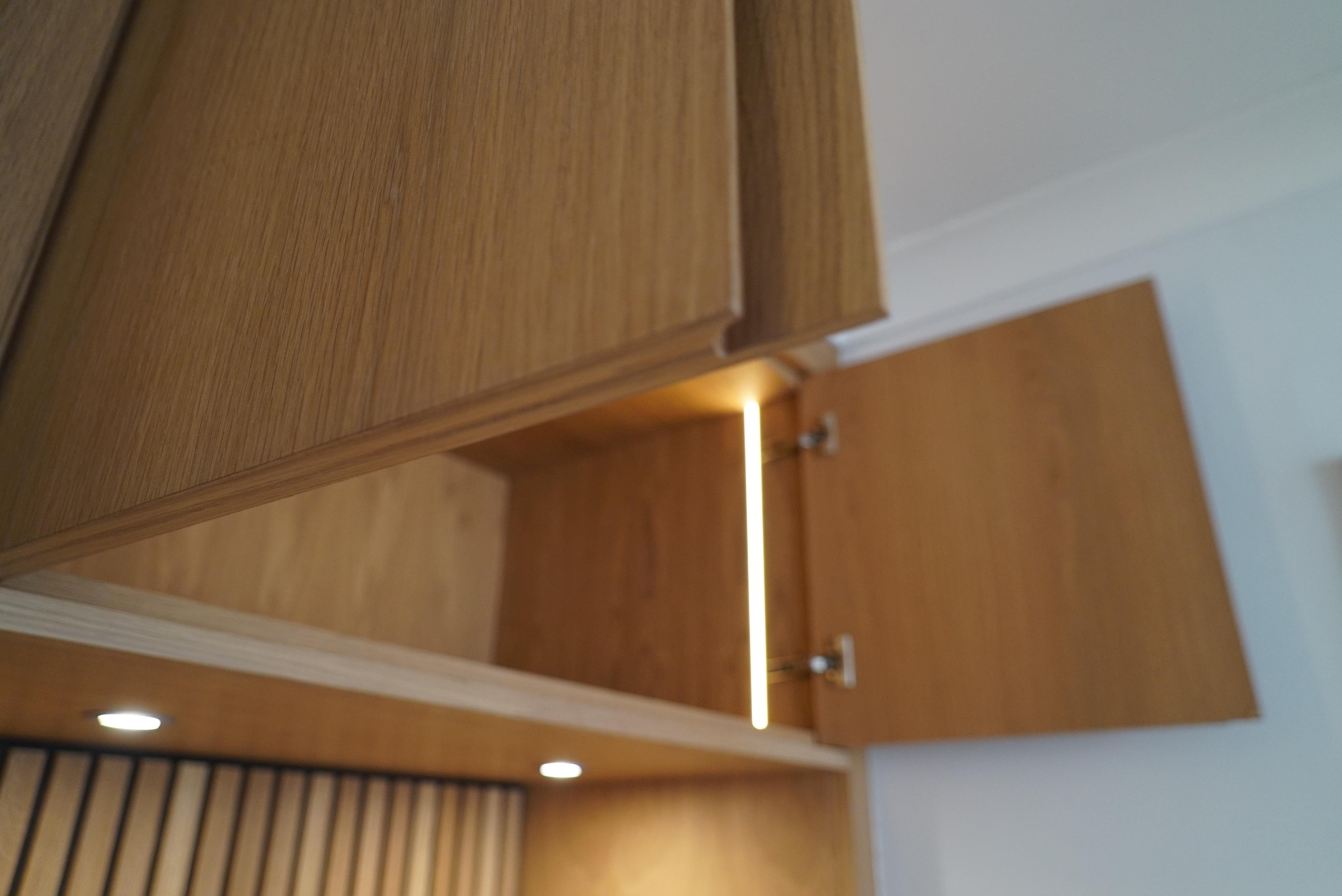 Wooden kitchen cabinet with open doors and interior lighting.