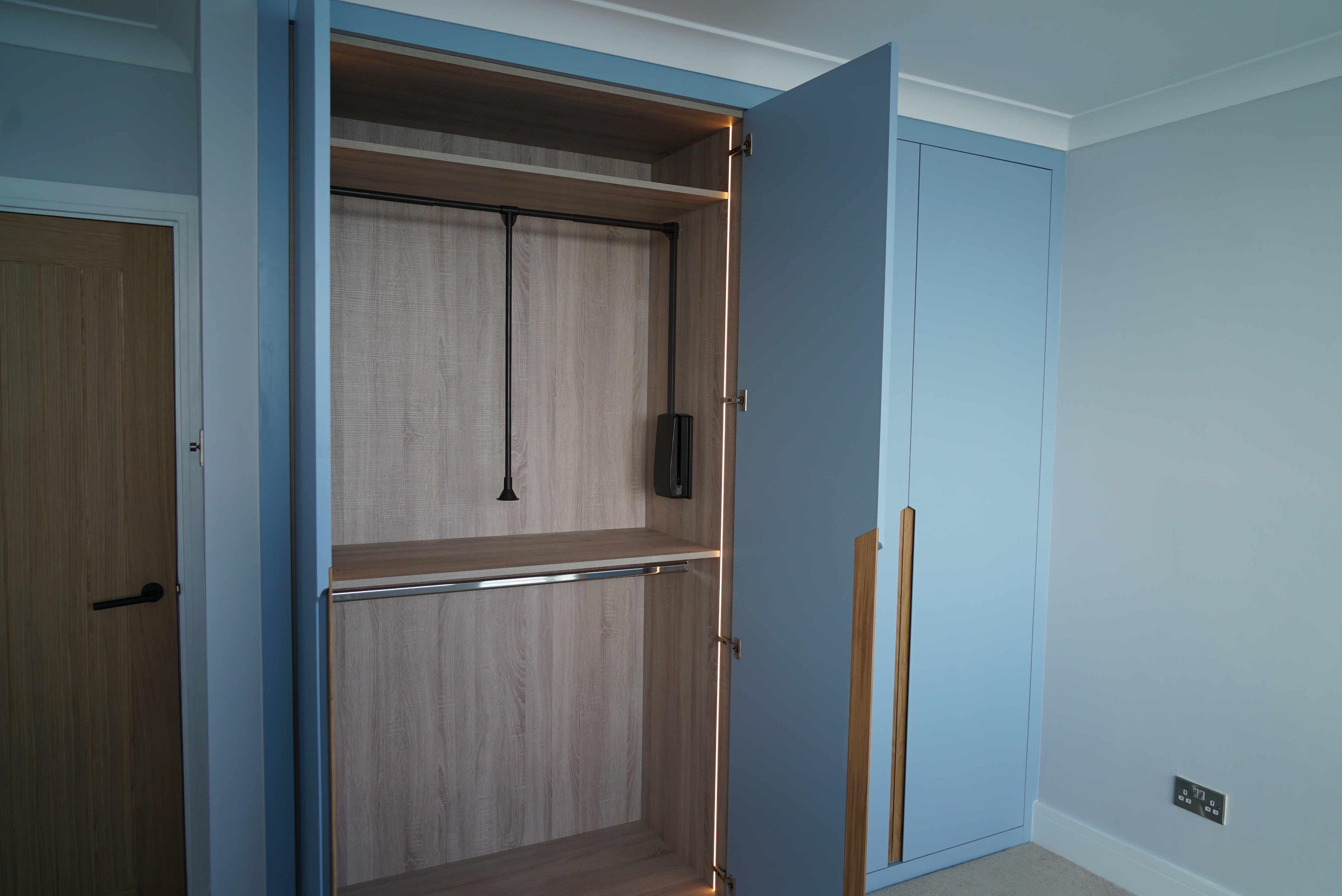 Open blue wardrobe with empty wooden interior and a hanging black cable inside a room.