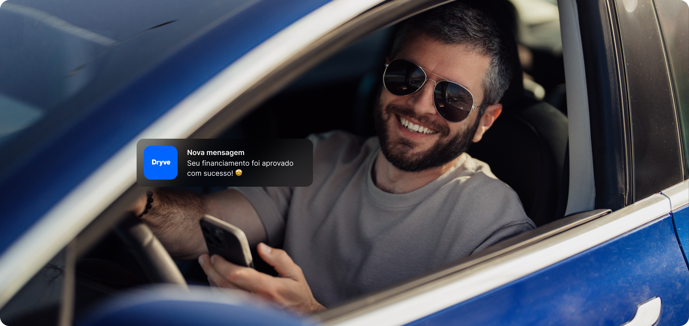 Homem feliz dentro de um carro recém-financiado, segurando o celular com uma notificação de aprovação da Dryve, representando um processo de financiamento de veículos sem burocracia.