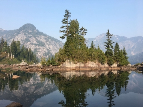 Photo by Greg of rocks, trees and mountains reflecting in still water