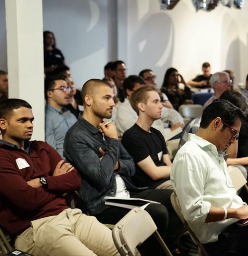 Meeting room full of guests and learners taking notes.