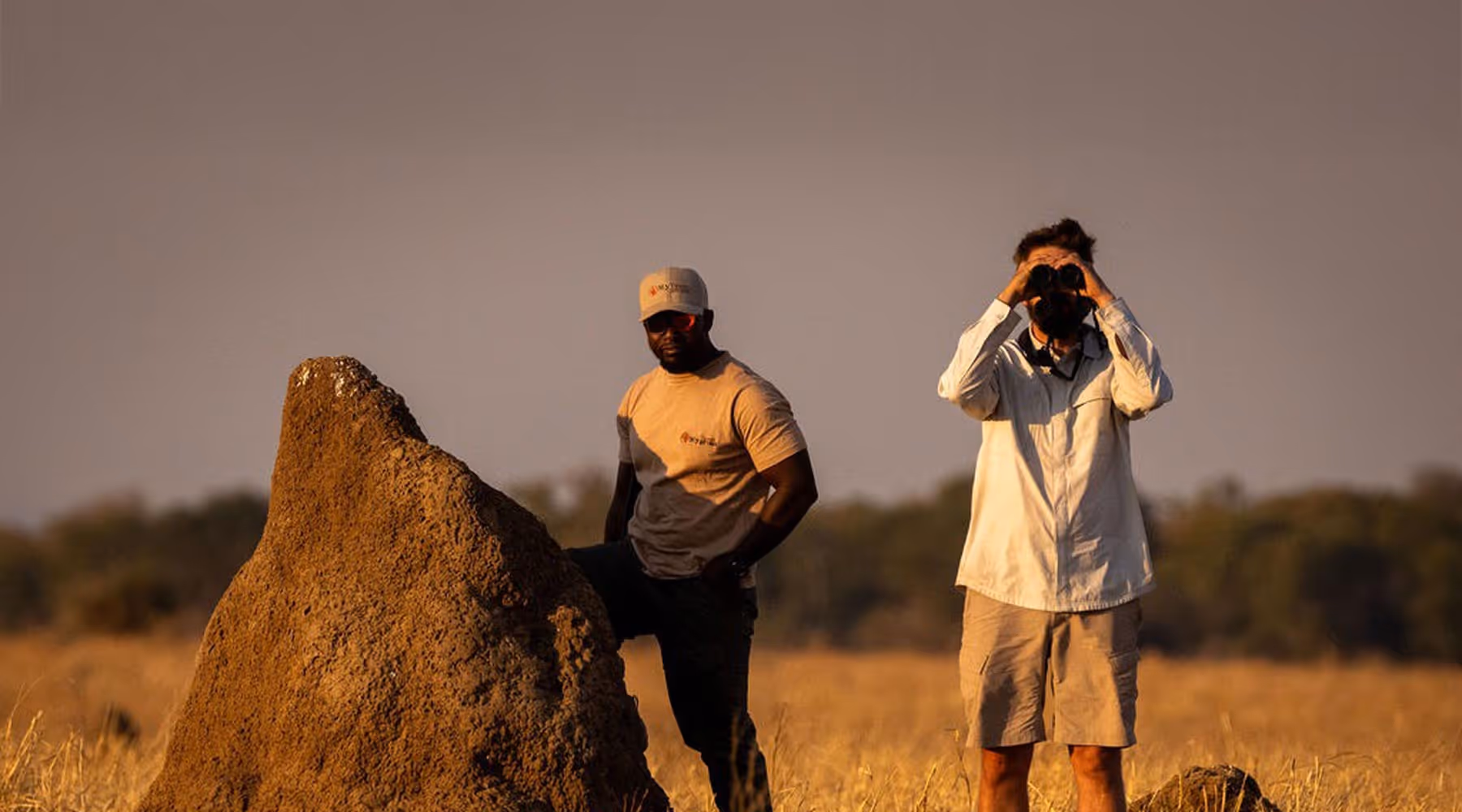 Two men in a field. One looking through binoculars.
