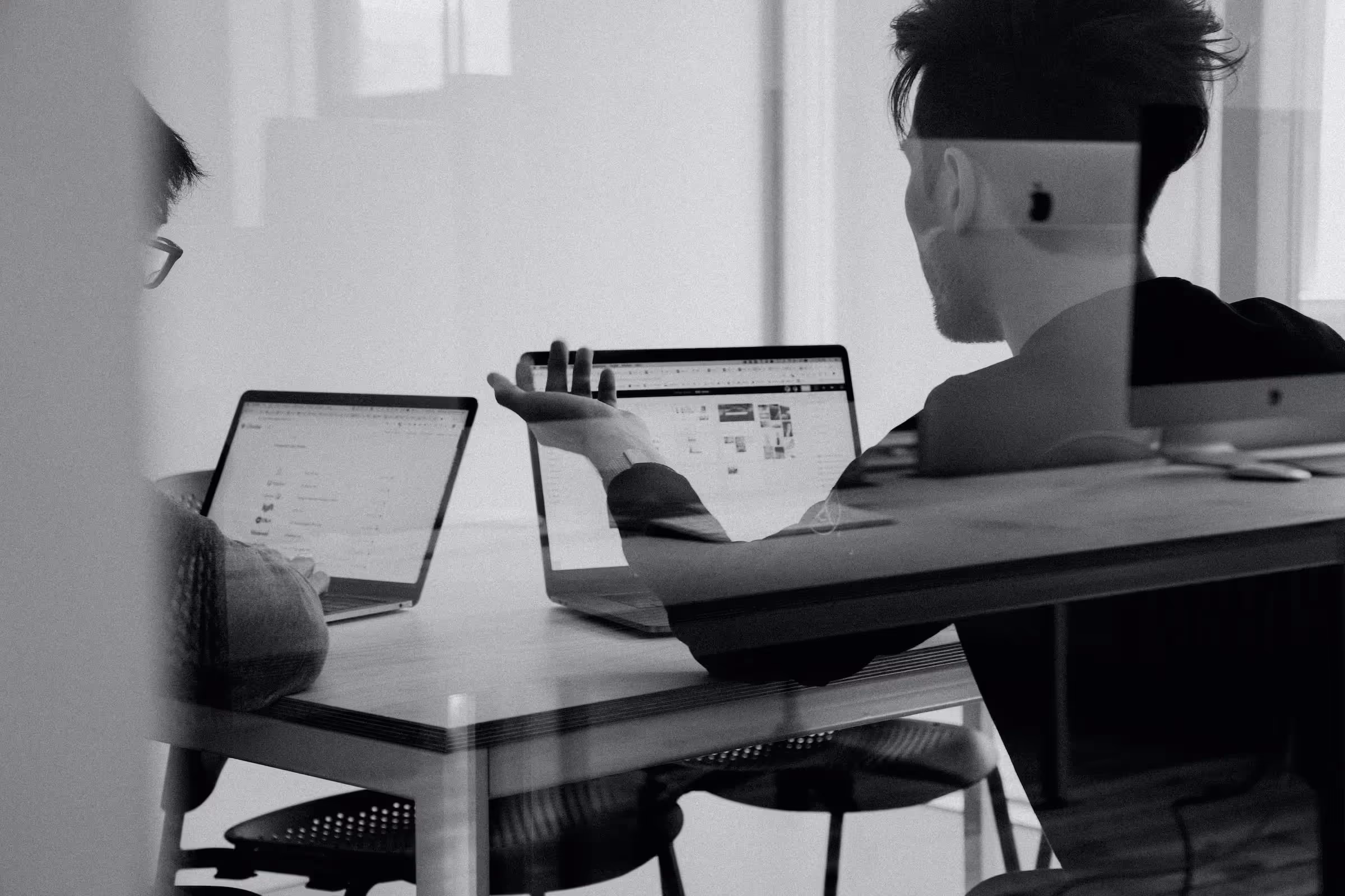 Two men talking in front of laptops in an office environment
