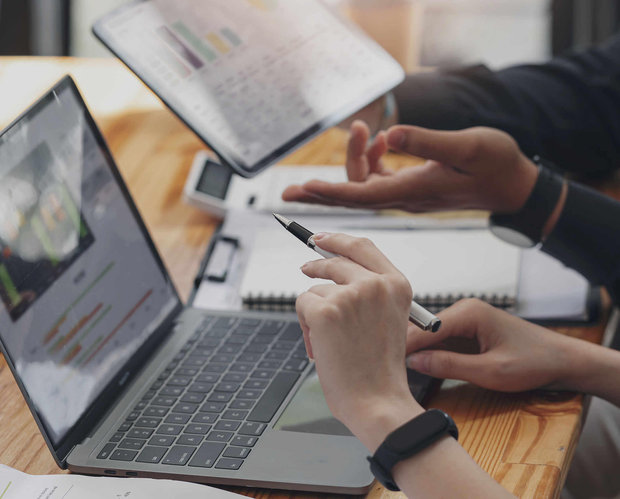 Hands reviewing analytics on a laptop and tablet during a business meeting