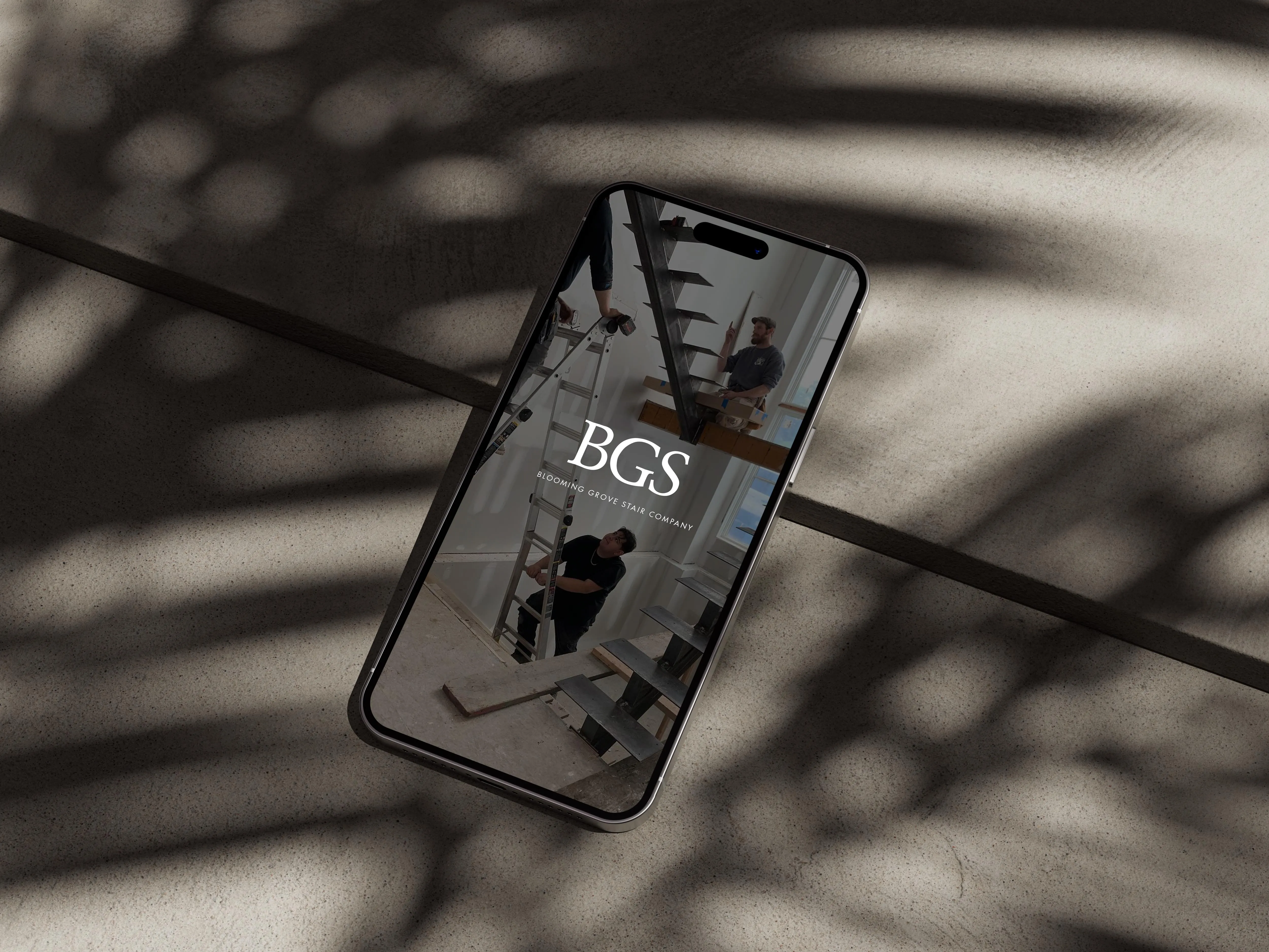 BGS website on an iPhone 14 Pro Max lying on concrete in palm shadows
