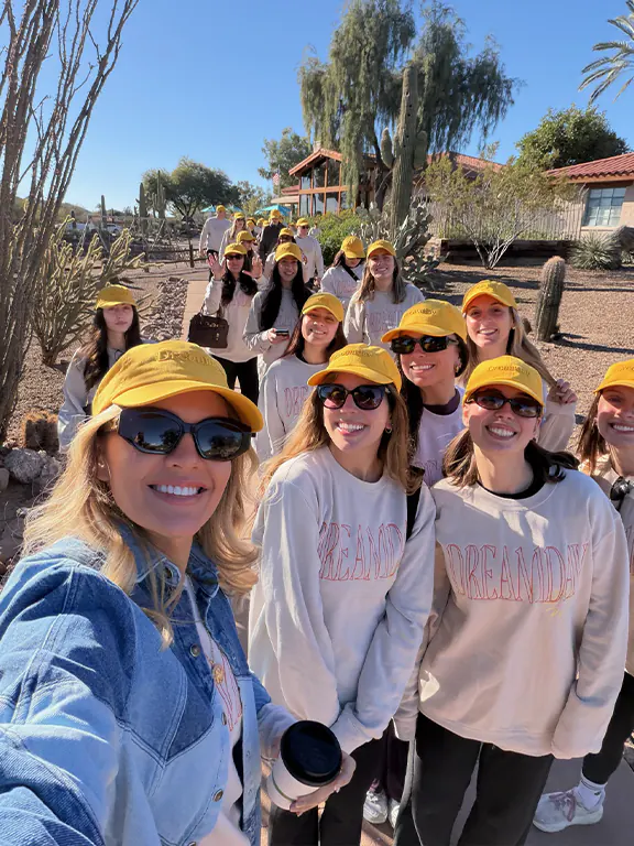 Dreamday Offsite 2026. Women wearing yellow hats and matching sweatshirts smiling outdoors on a sunny day.