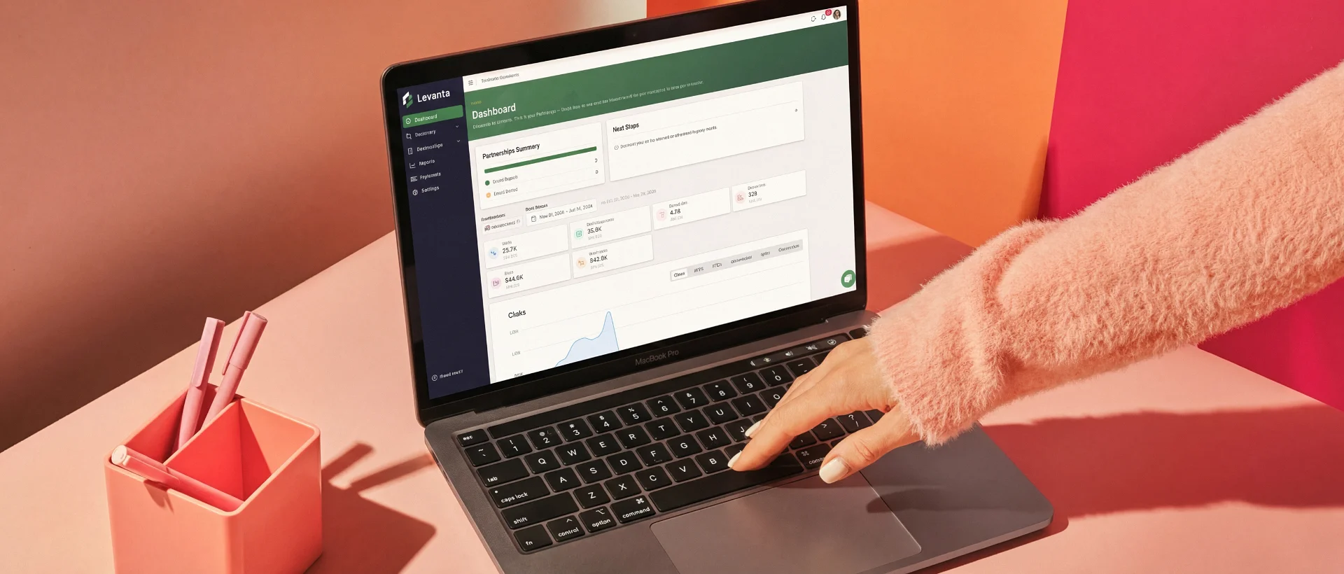Hand typing on MacBook Pro laptop showing Levanta app dashboard with data and charts on screen.