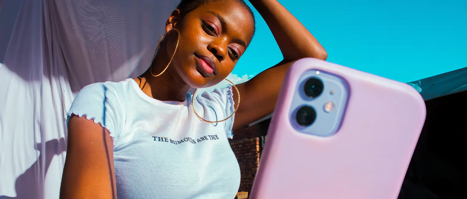Young woman with large hoop earrings taking a selfie outdoors with a pink phone case.