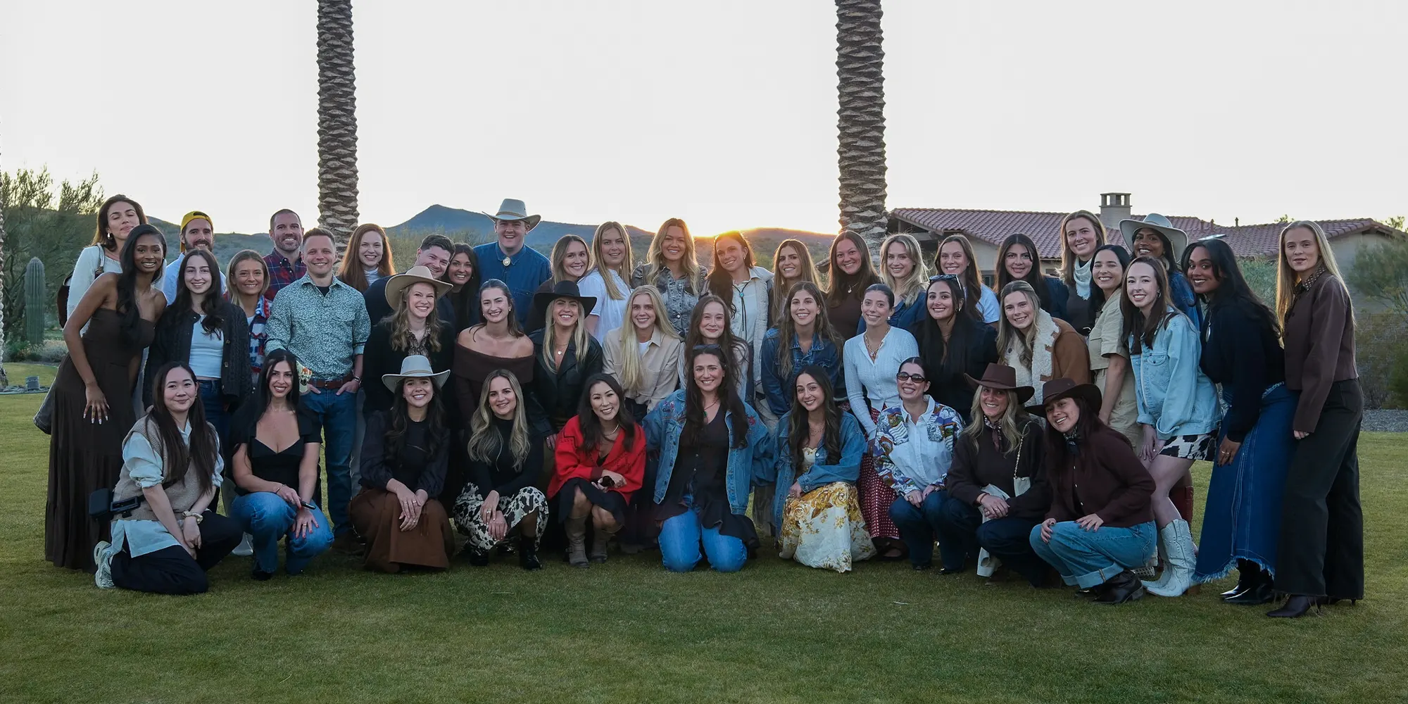 The Dreamday Team on their annual offsite (2026) posing together outdoors on grass near palm trees at sunset.