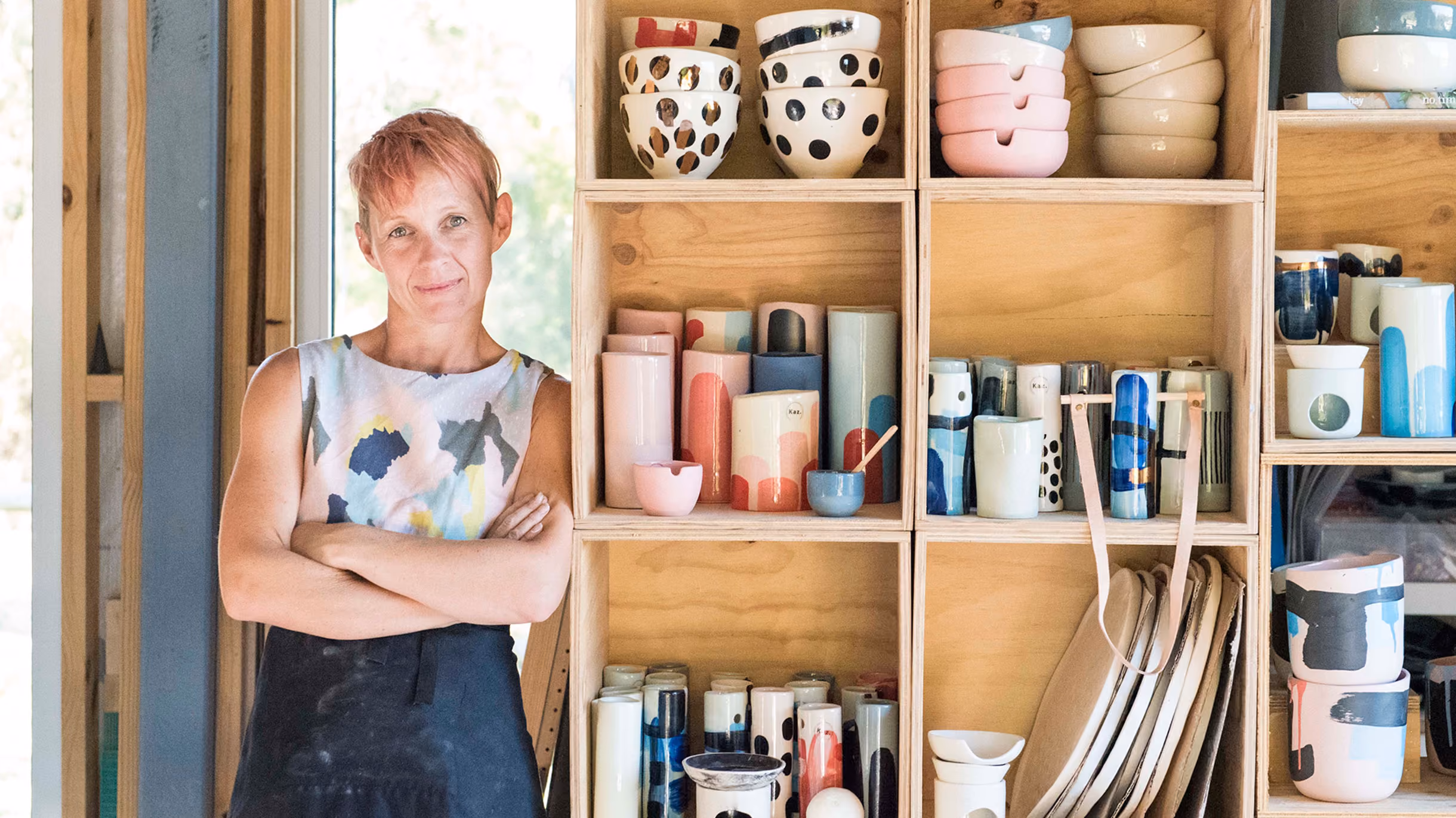 Karen Morton from Kaz Ceramics leans against shelves filled with pottery