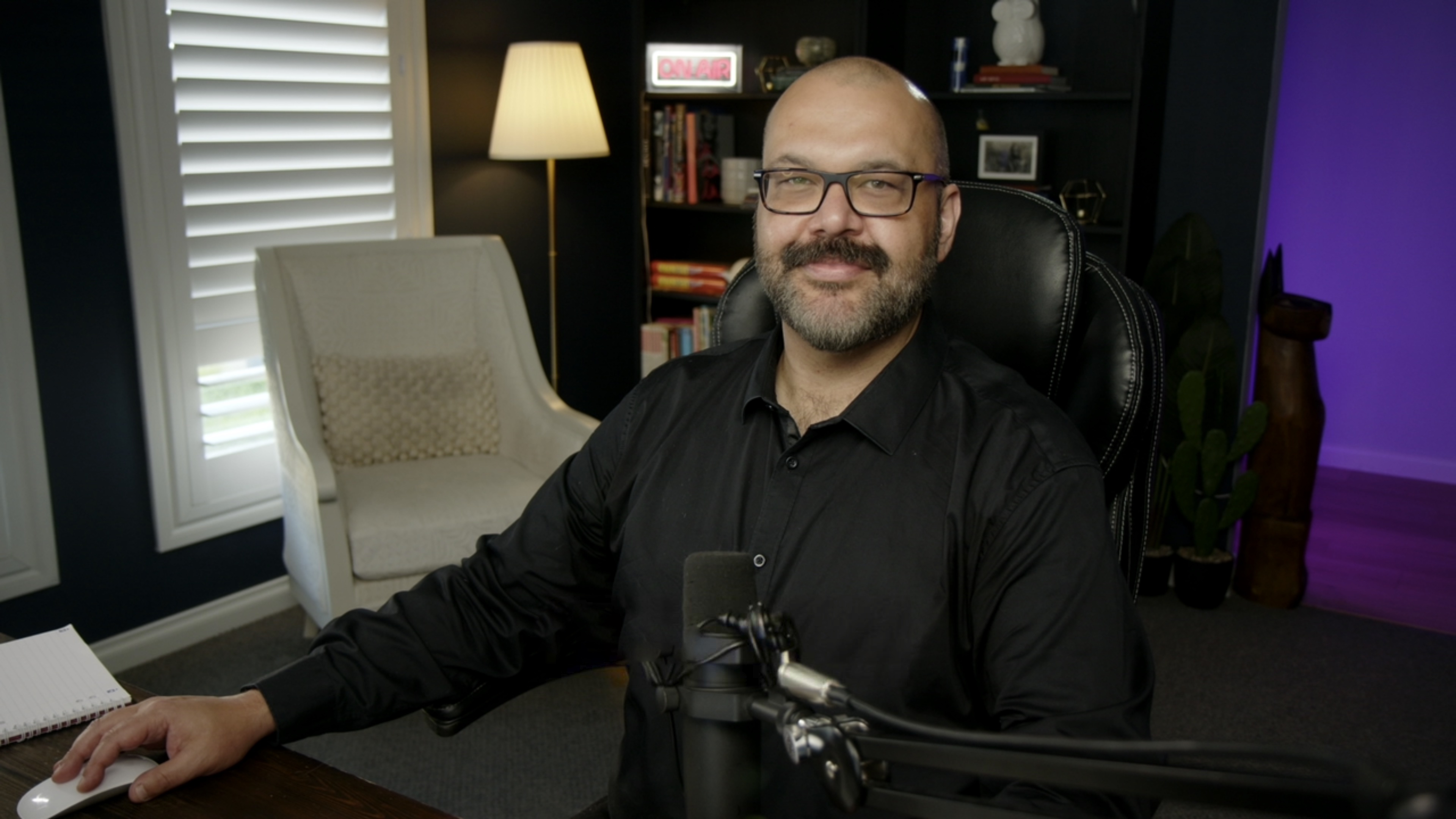 Nathan Little sitting at a podcast desk with a microphone, smiling.