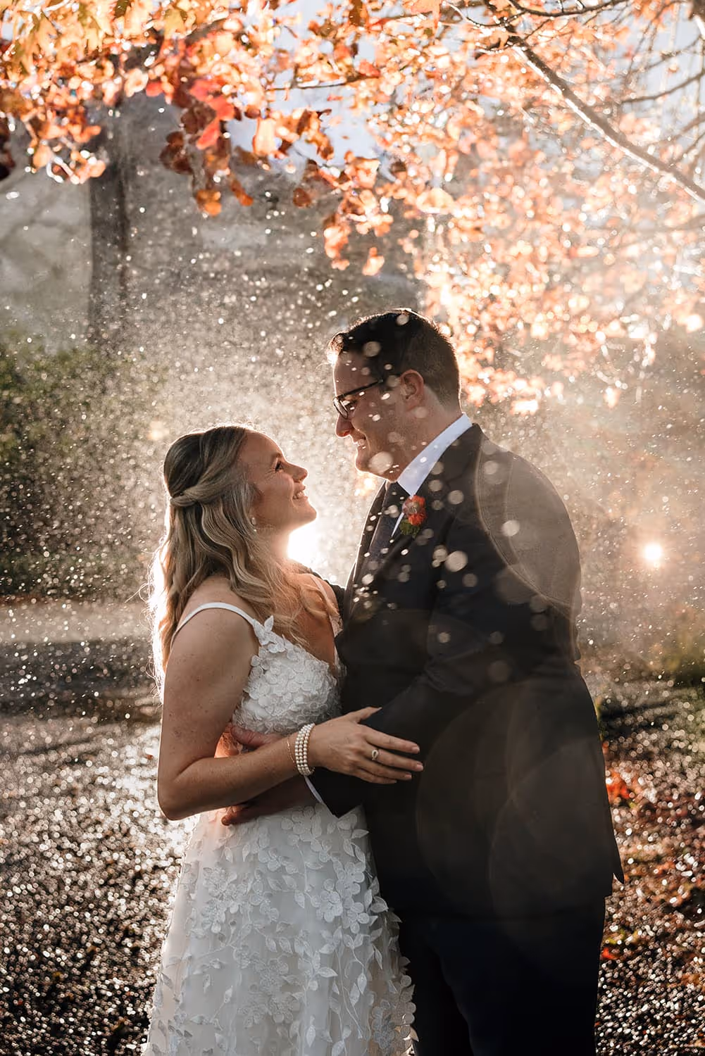 Romantic photograph of bride and groom, Sarah and Tate, embraced in a rain shower beneath autumn leaves at Kumeu Valley Estate. Beautifully captured by Amber at Perspectives Photography.
