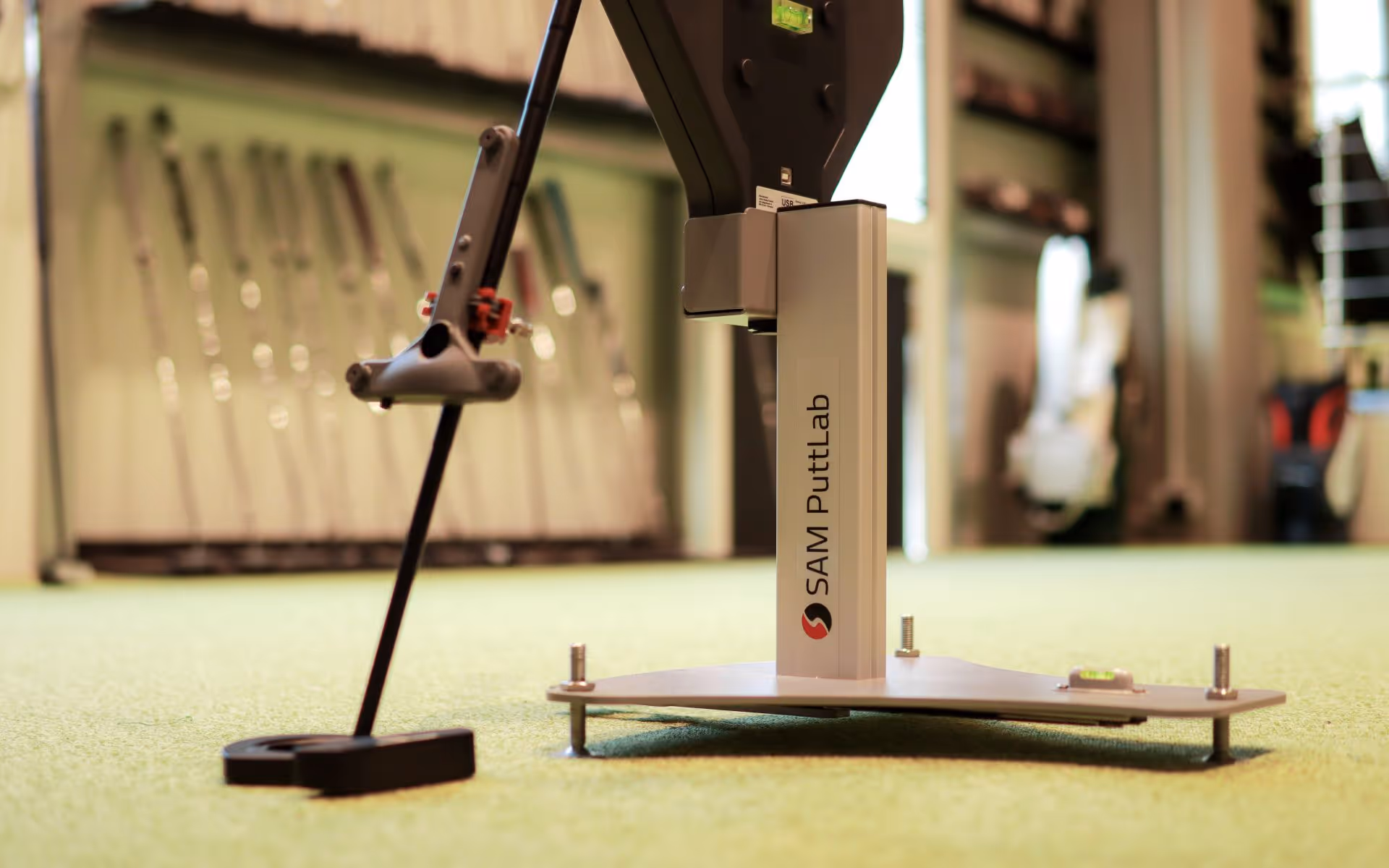 SAM PuttLab Gerät zur Analyse von Golfschlägerbewegungen auf einem grünen Teppichboden in einem Golfstudio.