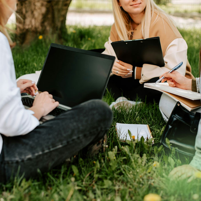Three girls with books, notebooks and laptop in a park