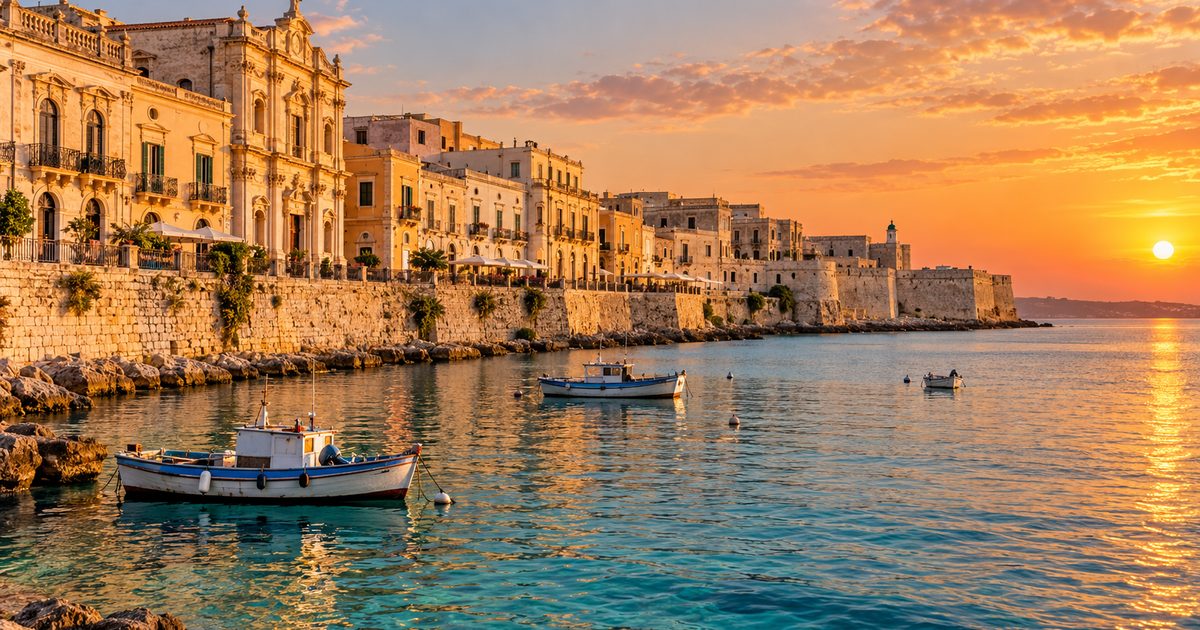 Lungomare di Ortigia a Siracusa al tramonto, con palazzi in pietra chiara e barche da pesca sul mare