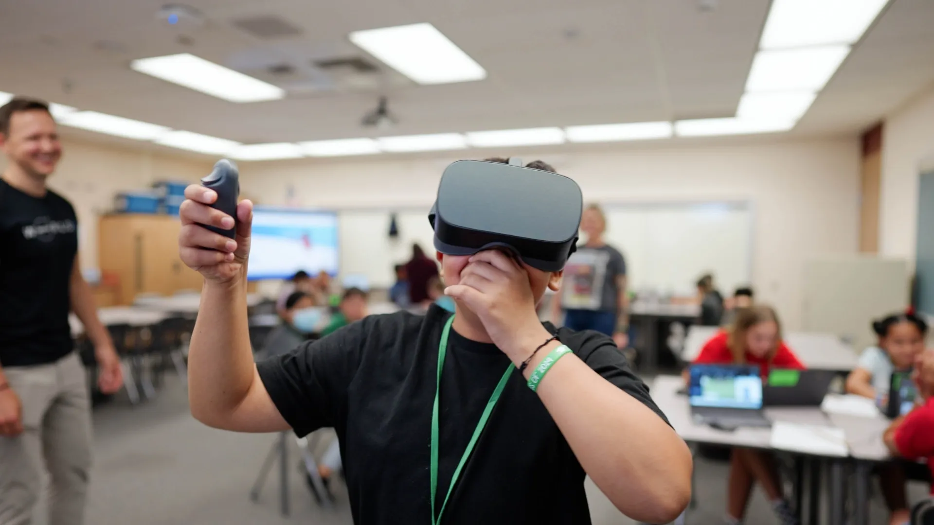 Hello World CS - A photo of a boy in a classroom wearing a VR headset with his hand raised to his mouth in delight as teachers look on smiling. Hello World CS is a tech investment by the Ruthless for Good Fund. 