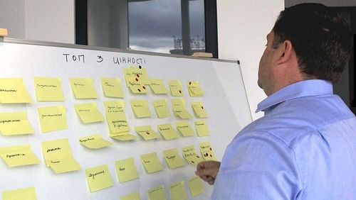 A person standing in front of a whiteboard with yellow sticky notes doing dot voting