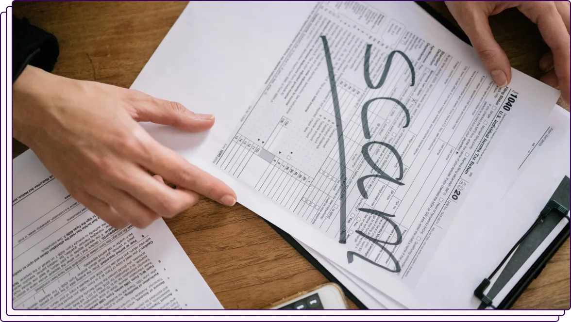 A person holding a document marked with the word "SCAM" written in large letters across the page. The document appears to resemble a tax or financial form, emphasizing fraud detection.