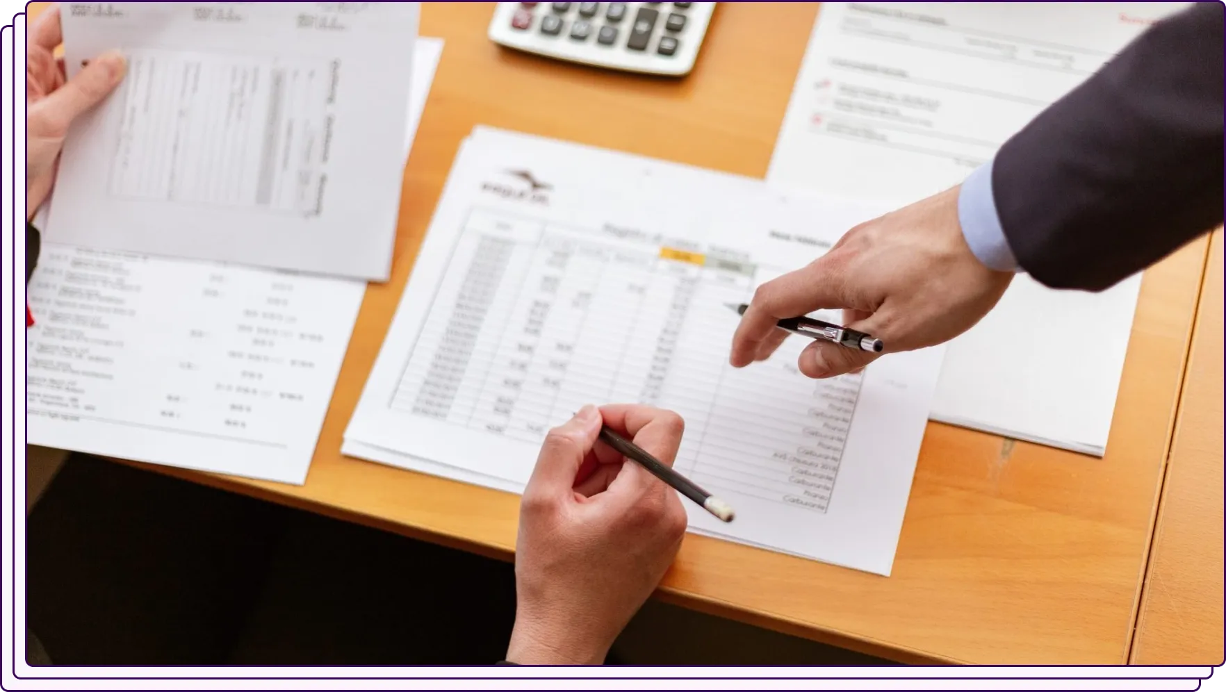 Two people reviewing printed documents at a desk, one pointing at a sheet with a pen while discussing the details. The setting reflects collaboration in fraud verification or document analysis.
