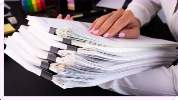 A close-up of a stack of paper documents clipped together with large binder clips, being handled by a person. The image reflects manual document organization or review, possibly for compliance or inspection purposes.