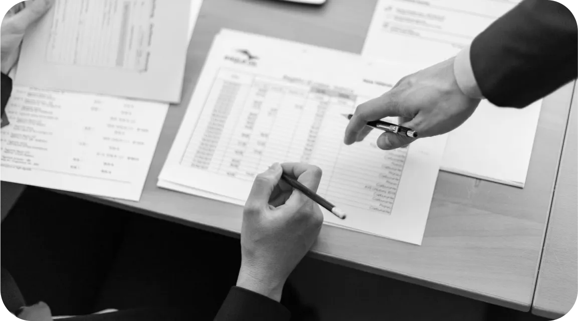 Two individuals reviewing printed financial statements at a desk, pointing to a spreadsheet—representing detailed examination of formatting, calculations, and inconsistencies in a pay stub.