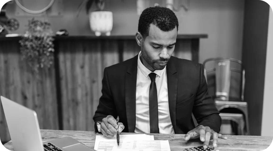 Business professional in a suit reviewing financial documents and using a calculator, representing manual document review for W-2 fraud detection.