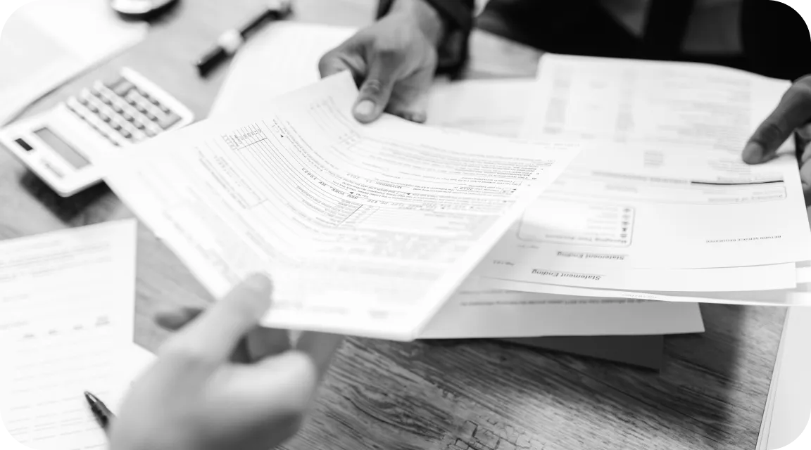 Close-up of two professionals reviewing tax forms at a desk, with hands holding documents like W-2s and 1099s, a calculator and pen in the background—representing financial document verification during loan applications.