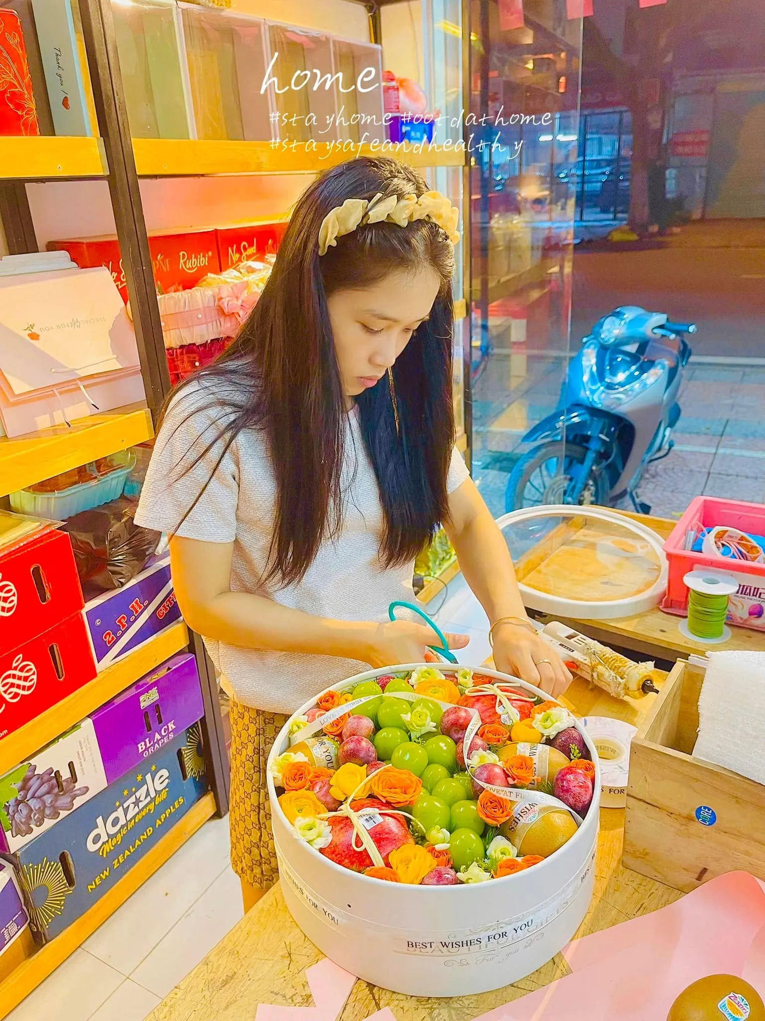Nữ nhân viên trang trí giỏ hoa quả tròn trong hộp trắng tại cửa hàng tạp hóa — King Fruit thị xã Ba Đồn, Quảng Bình