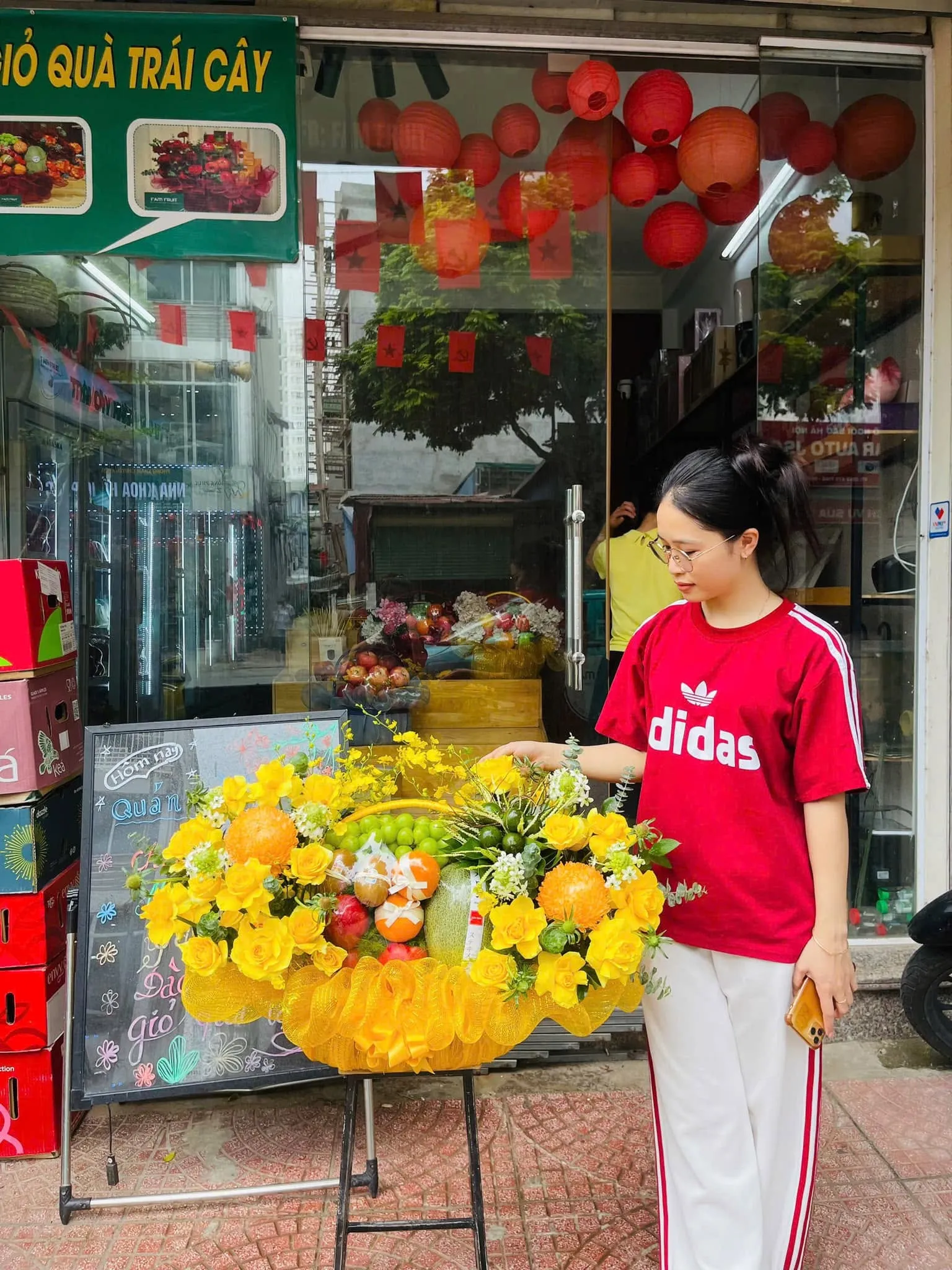 Cô gái chỉnh giỏ hoa quả vàng trước cửa hàng giỏ quà trái cây có đèn lồng đỏ — King Fruit thị xã Ba Đồn, Quảng Bình